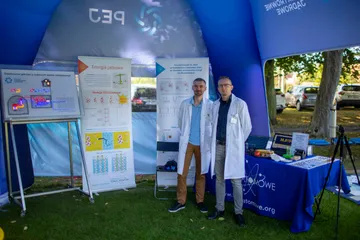 Dwie osoby w białych fartuchach przy stoisku Fundacji w niebieskim namiocie, obok plansze o energii jądrowej