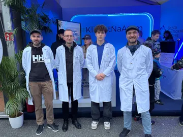 Cztery osoby w białych fartuchach przed stoiskiem Polskich Elektrowni Jądrowych