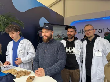 Cztery osoby, trzy w białych fartuchach, przy stole stoiska z napisem #KlimatNaAtom