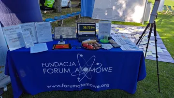 Stół Fundacji z niebieskim obrusem z logo; na stole ulotki, laptop, owoce i urządzenie pomiarowe z wyświetlaczem
