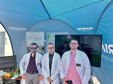 Trzy osoby w białych fartuchach w namiocie Industria przy stoisku Fundacji z ekranem