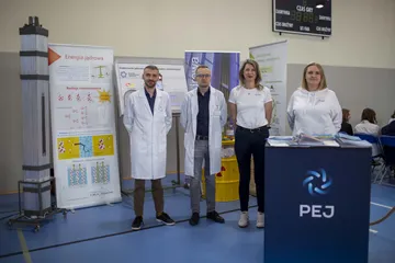 Cztery osoby przy stoisku Fundacji i Polskich Elektrowni Jądrowych, obok plansze o energii jądrowej i model kasety paliwowej
