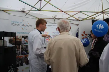 Osoba z Fundacji rozmawia ze starszym zwiedzającym przy planszy