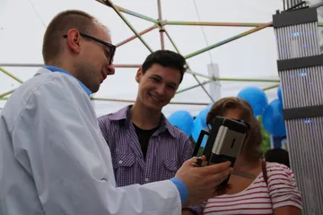 Osoba w białym fartuchu pokazuje zwiedzającym miernik promieniowania