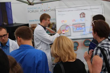 Osoba w białym fartuchu objaśnia zwiedzającym podświetlany model elektrowni jądrowej