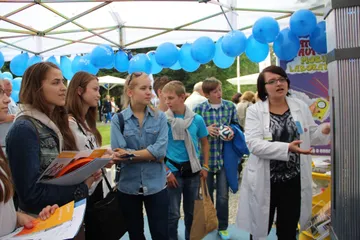 Grupa młodzieży z materiałami przy namiocie z niebieskimi balonami