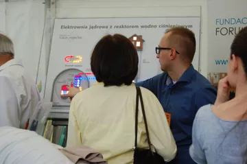 Osoba z Fundacji objaśnia zwiedzającej planszę o elektrowni jądrowej