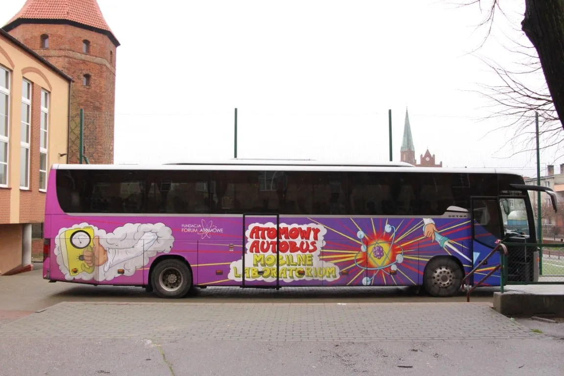 Fioletowy Atomowy Autobus przy szkole w Lęborku; w tle ceglany kościół