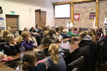 Spotkanie w sali obrad z godłem i flagą; słuchacze przy stołach