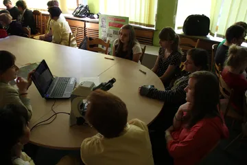 Uczestnicy zajęć przy dużym stole z laptopem i mikroskopem