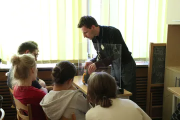 Osoba pokazuje młodzieży doświadczenie w szklanej osłonie przy stole