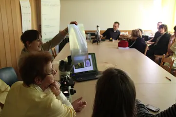 Uczestnicy zajęć przy stole z mikroskopem i laptopem; jedna osoba unosi kliszę pod światło