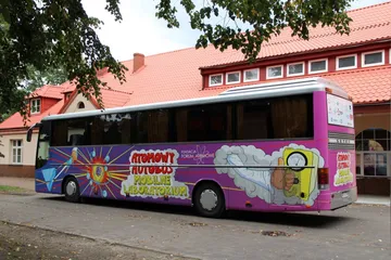 Atomowy Autobus przed budynkiem z czerwonym dachem