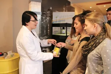 Osoba w białym fartuchu podaje uczennicom eksponat
