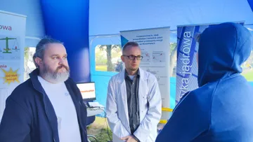 Osoba w białym fartuchu ze zwiedzającymi przy planszach o energii jądrowej