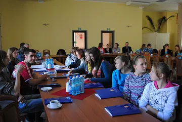 Młodzież przy długich stołach konferencyjnych z teczkami