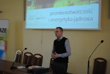 Prelegent przed ekranem z tytułem „Promieniotwórczość i energetyka jądrowa”