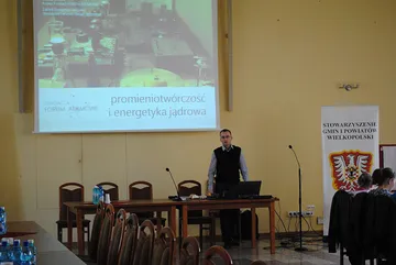 Prelegent w sali obrad; na ekranie tytuł wykładu, obok roll-up Stowarzyszenia Gmin i Powiatów Wielkopolski