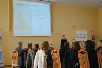 Uczestnicy słuchają wykładu; na ekranie slajd o okresie połowicznego rozpadu