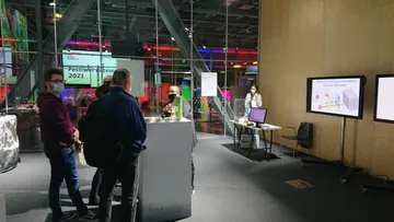 Stoisko Fundacji podczas Festiwalu Przemiany 2021: stolik z eksponatami, ekrany i zwiedzający