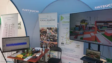 Stoisko Fundacji w namiocie: plansze, stolik z laptopem i owocami, ekran z modelem elektrowni jądrowej