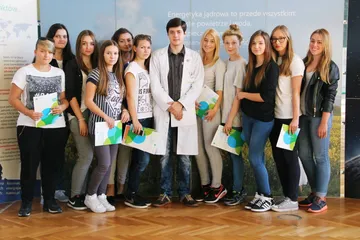 Grupa uczniów z broszurami pozuje z osobą w białym fartuchu