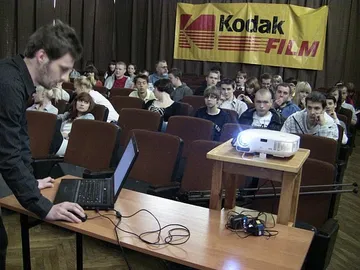 Osoba przy laptopie i projektorze; w tle uczniowie na widowni i baner Kodak Film