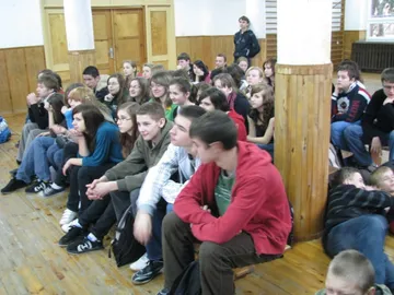 Gimnazjaliści siedzą na podłodze i ławkach w sali podczas wykładu