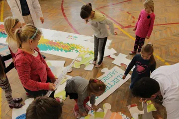 Dzieci układają na podłodze duże puzzle z elektrownią jądrową