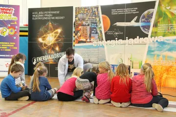 Dzieci siedzą na podłodze przed planszami o energii jądrowej