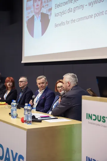 Uczestnicy panelu za stołem prelegentów; na ekranie slajd o korzyściach elektrowni jądrowej dla gminy