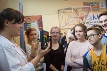 Osoba w białym fartuchu pokazuje uczniom miernik promieniowania