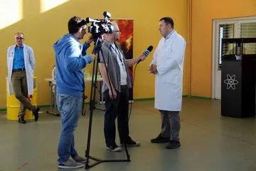 Ekipa telewizyjna nagrywa wywiad z osobą w białym fartuchu w sali gimnastycznej