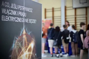 Uczniowie w sali gimnastycznej obok planszy „A co, jeśli pstrykniesz włącznik i prądu elektrycznego nie będzie?”