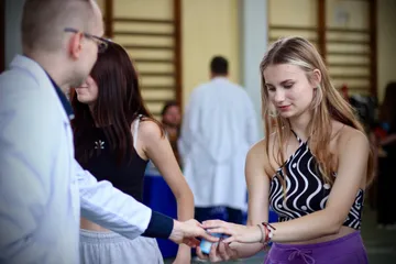 Uczennica dotyka eksponatu przy stoisku; obok osoba w białym fartuchu
