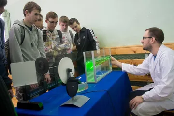 Osoba w białym fartuchu prowadzi doświadczenie z laserem przed uczniami