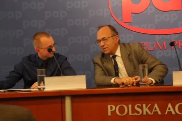 Uczestnicy konferencji prasowej rozmawiają za stołem z mikrofonami na tle logo PAP