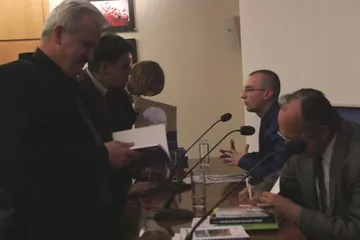 Uczestnicy konferencji przeglądają materiały przy stole prezydialnym