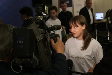 Osoba w białej koszulce Fundacji udziela wywiadu przed kamerą