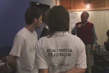 Osoba w koszulce z napisem „Atom i wiedza tylko razem” i logo Fundacji, stojąca tyłem do aparatu