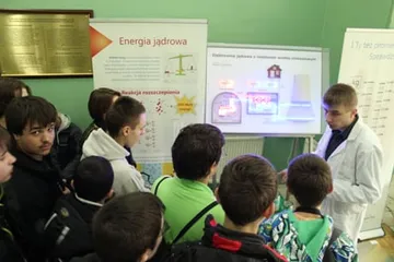 Uczniowie przed planszą „Energia jądrowa”; obok osoba w białym fartuchu