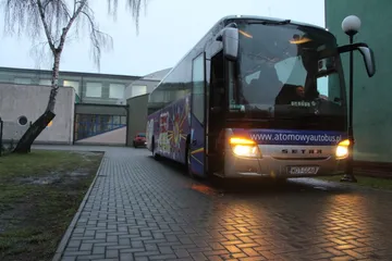 Atomowy Autobus z włączonymi światłami przed szkołą o zmierzchu