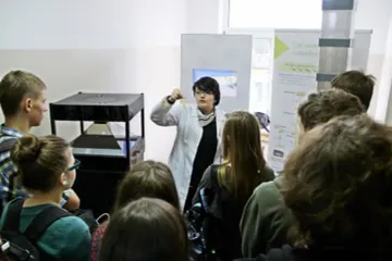 Osoba w białym fartuchu objaśnia uczniom eksponat