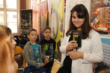 Osoba w białym fartuchu pokazuje dzieciom miernik promieniowania