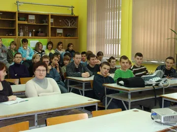 Uczniowie liceum w ławkach pracowni fizycznej słuchają wykładu; na pierwszym planie projektor