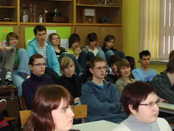Uczniowie liceum słuchają wykładu, część siedzi na szafkach pod ścianą