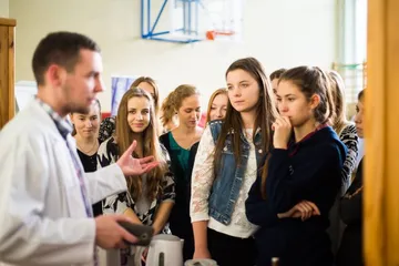 Osoba w białym fartuchu opowiada grupie uczennic