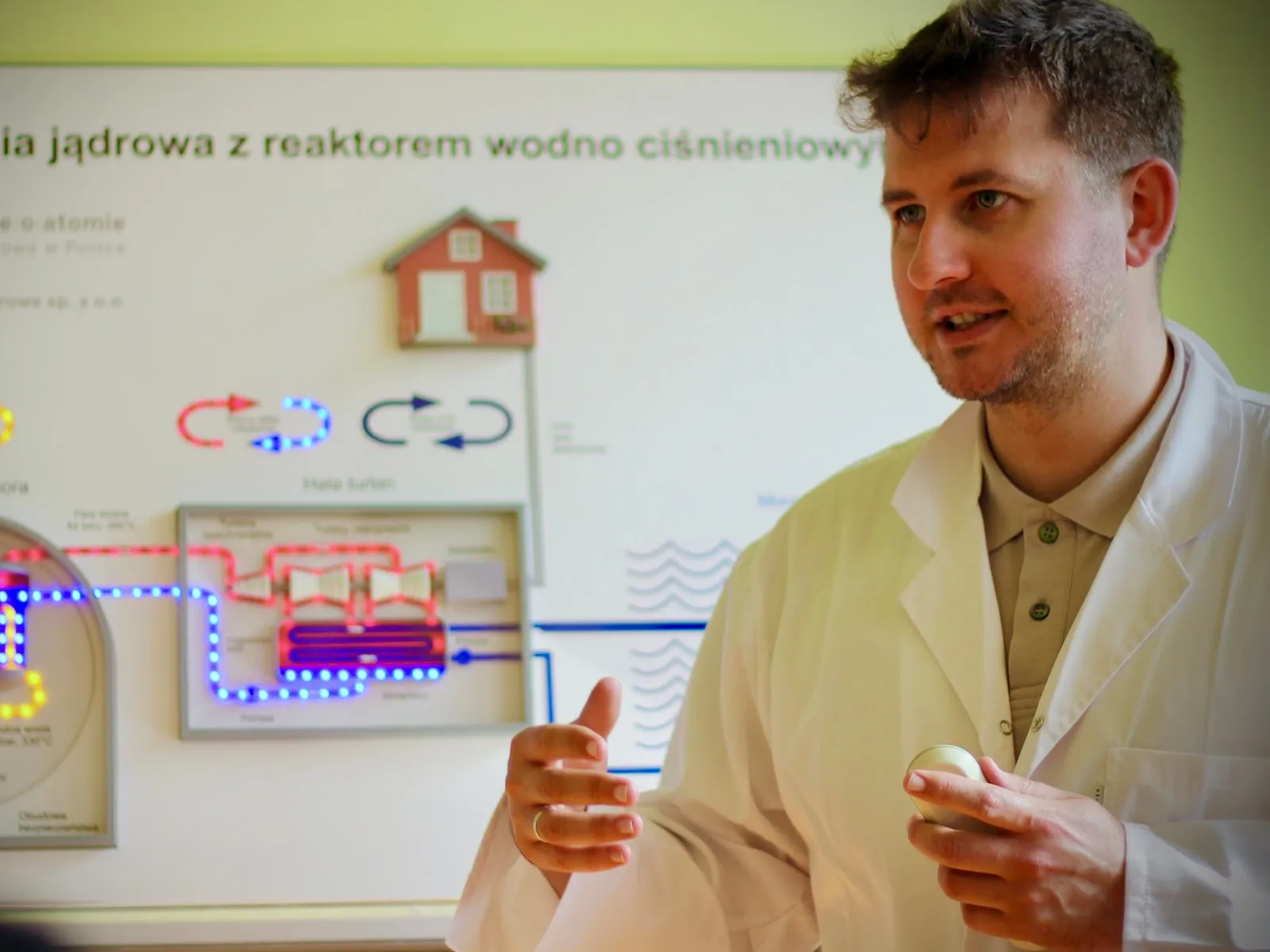 Osoba z zespołu Fundacji w fartuchu laboratoryjnym objaśnia podświetlany schemat elektrowni jądrowej z reaktorem wodno-ciśnieniowym