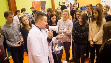 Osoba w białym fartuchu z megafonem przed grupą uczniów