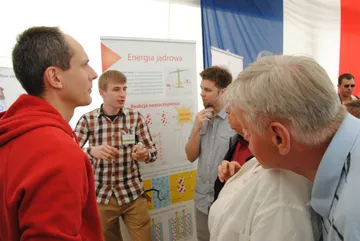 Osoba z Fundacji rozmawia ze zwiedzającymi przy planszy „Energia jądrowa”